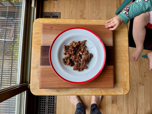 Plate of food on a wooden tray with a child's hand reaching out